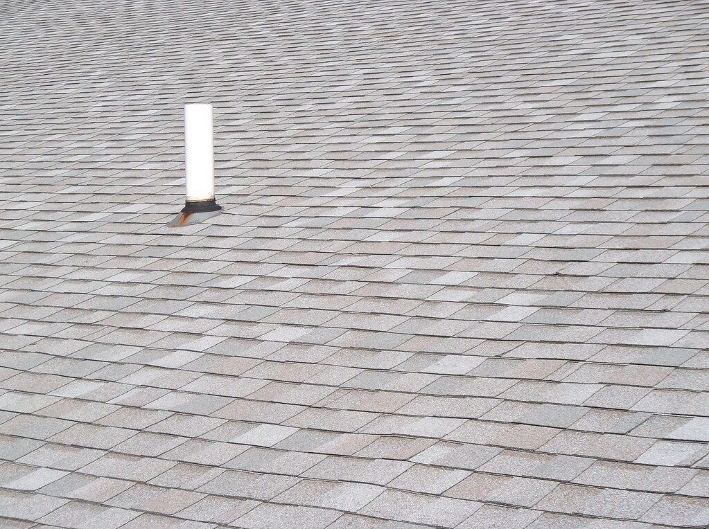 A white post on grey shingles, which is what the eye lands on before the mind says “roof vent.”