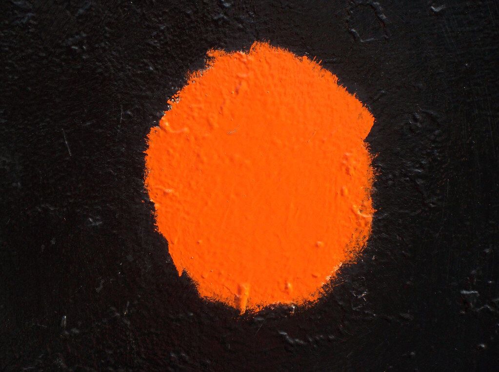 An orange disc on a black wall. Color and dot arrive together, and the color wins.