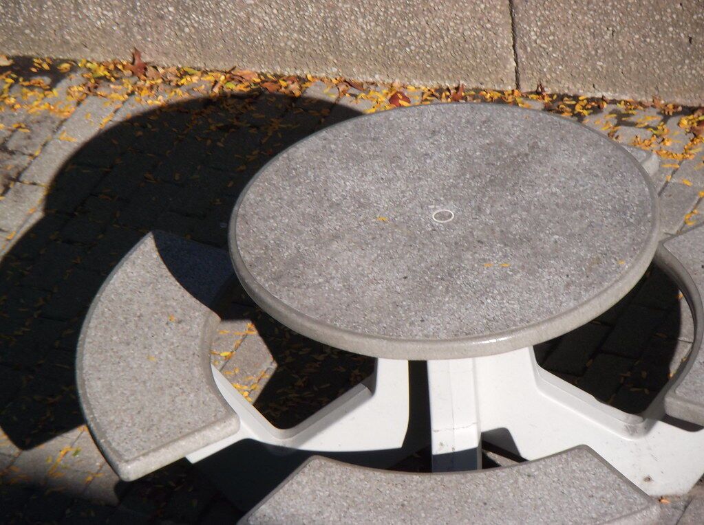 A concrete table in sun, all shape and shadow before the word “table.”